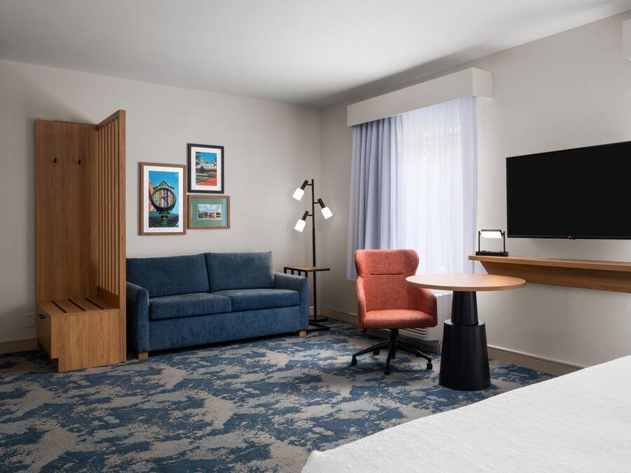 A hotel room with a blue sofa, a wooden cabinet, a round table, a TV, and artwork on the wall.