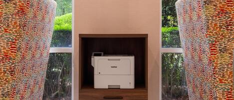 A modern room with a printer in a wooden cabinet, large windows, and patterned furniture.