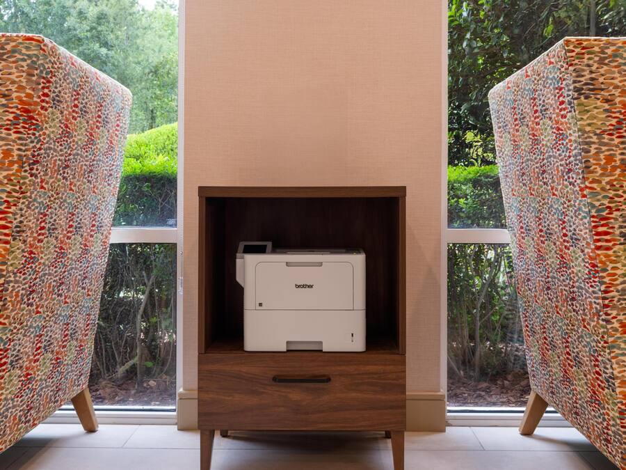 Ein modernes Zimmer mit Drucker in einem Holzkabinett, großen Fenstern und Möbeln mit Muster.