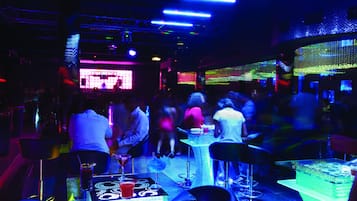 Un espace bar avec des tables et des chaises, une scène avec un DJ et une foule de personnes.