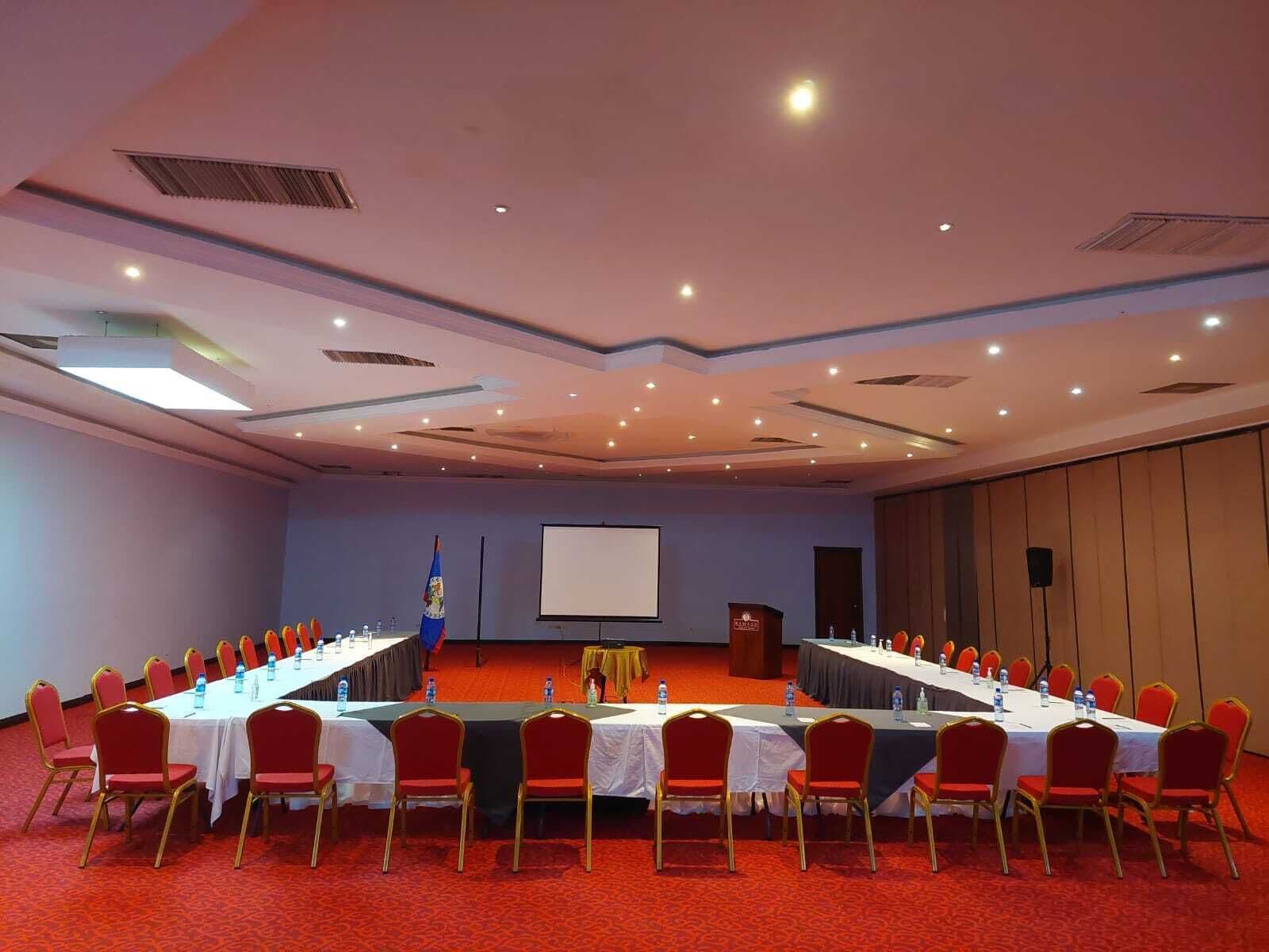 A conference room with a long table, red chairs, and a projector screen.