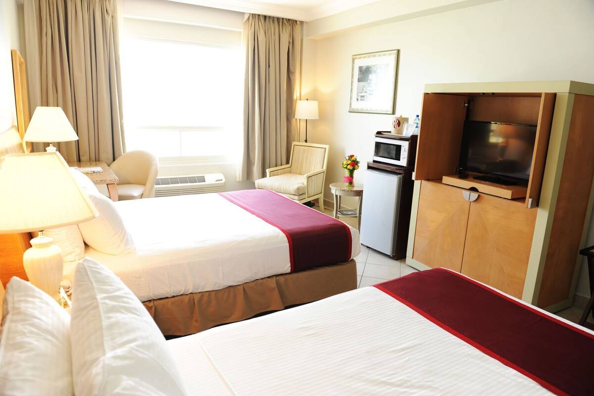 Hotelkamer met een bed, nachtkastje, lamp, stoel, bureau, magnetron, koelkast, televisie en gordijnen.