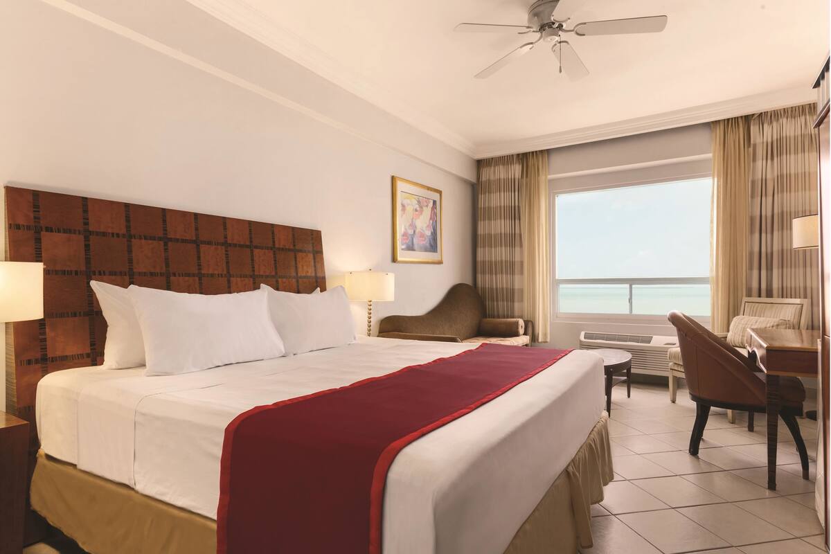 Een hotelkamer met een groot bed, een bureau, een stoel en uitzicht op de oceaan.