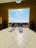A balcony with two chairs, a tiled floor, and a view of the sky and distant landscape.