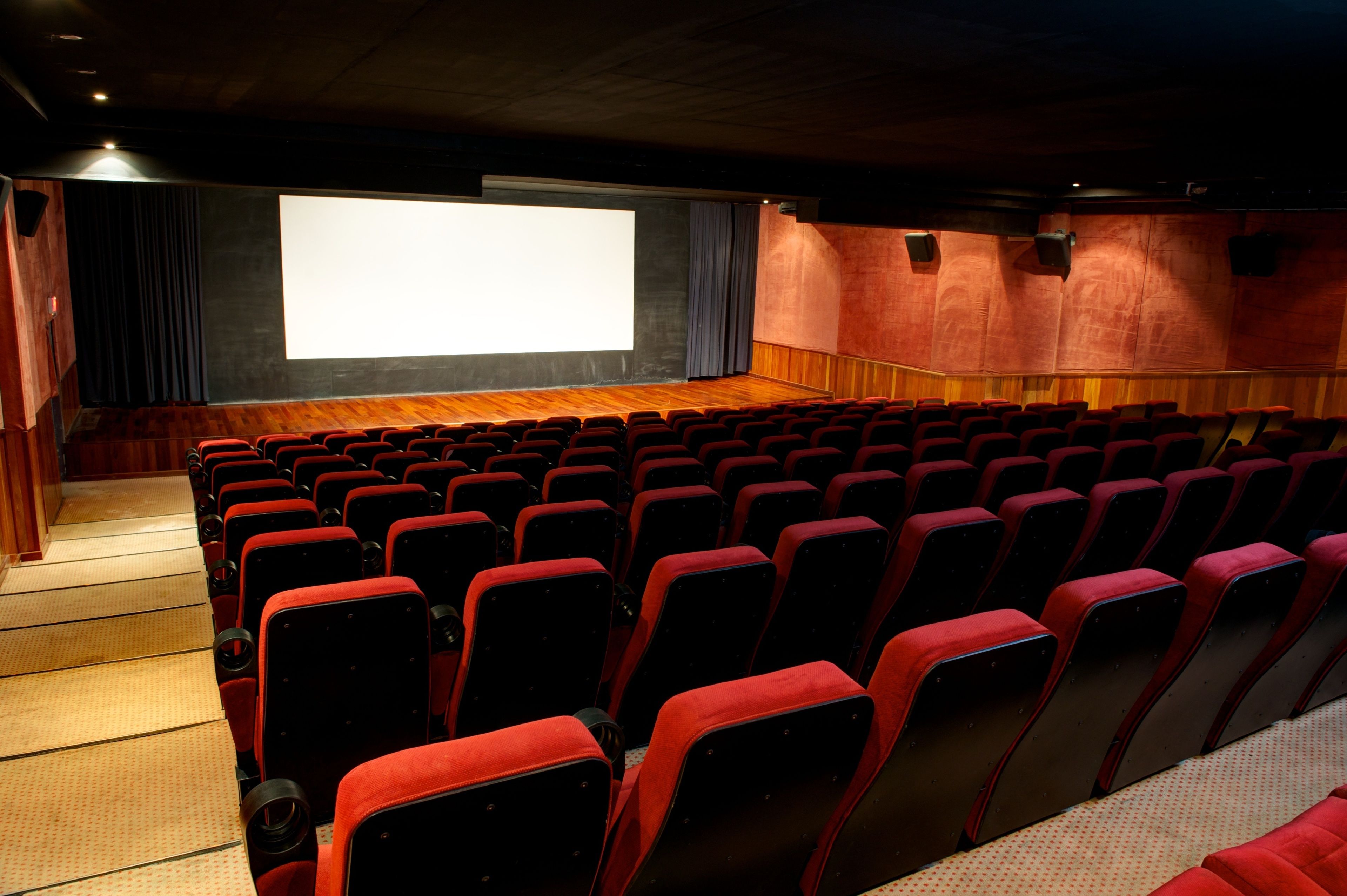 An empty movie theater with rows of red seats and a large screen at the front.