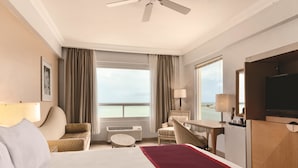 Habitación de hotel con cama, escritorio, silla, televisor y vista al mar.