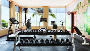 Un gimnasio con equipo de ejercicio, ventanas grandes y un mural.