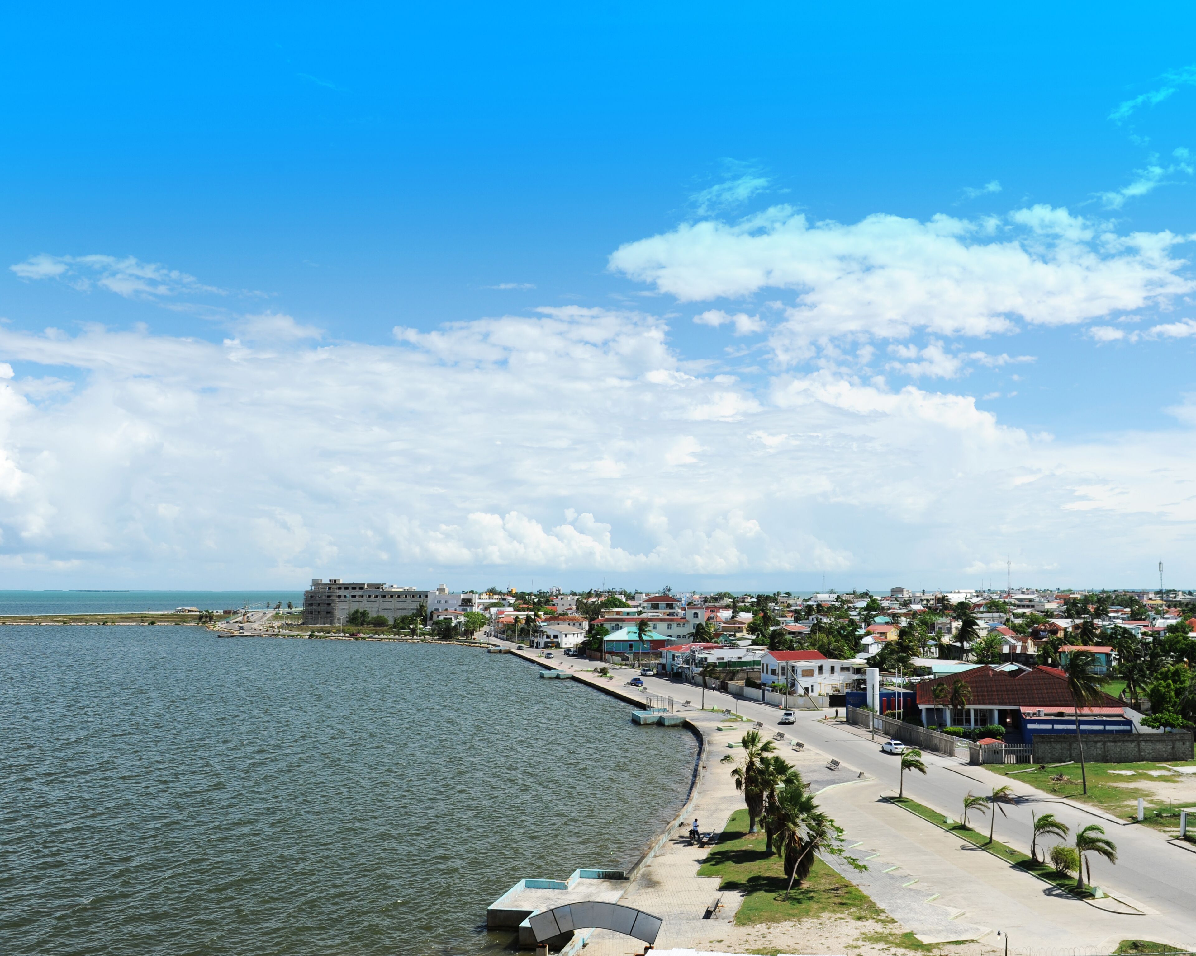 Un paisaje urbano costero con un paseo marítimo, edificios y un cielo despejado.