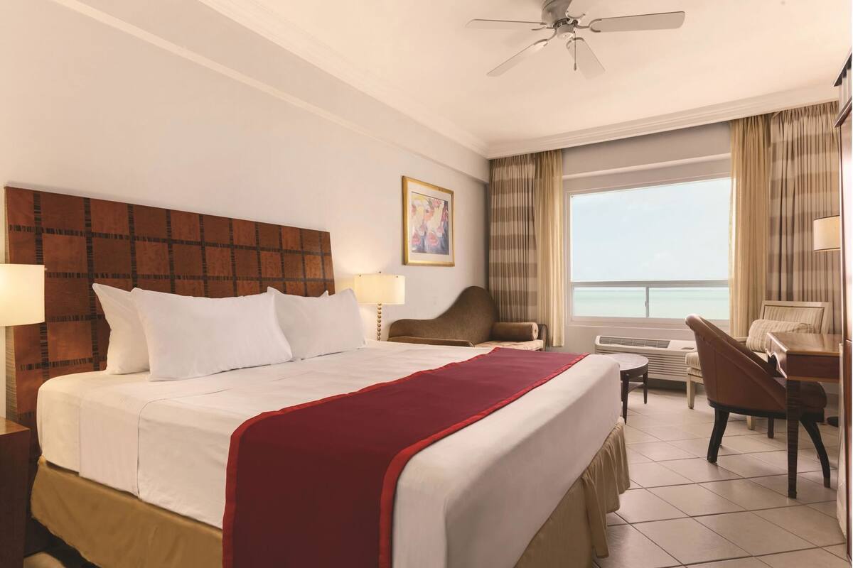 Een hotelkamer met een bed, een bureau, een stoel, een plafondventilator en een raam met uitzicht.