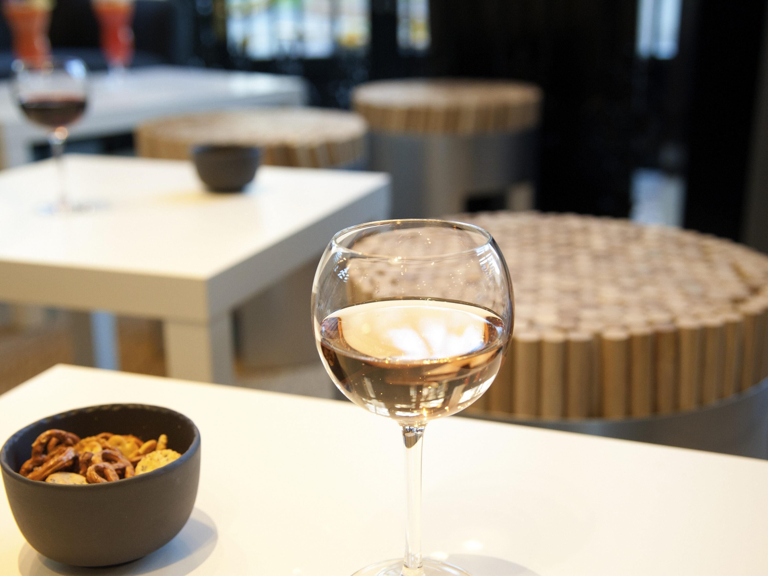 A glass of white wine on a table with a bowl of snacks in the foreground.