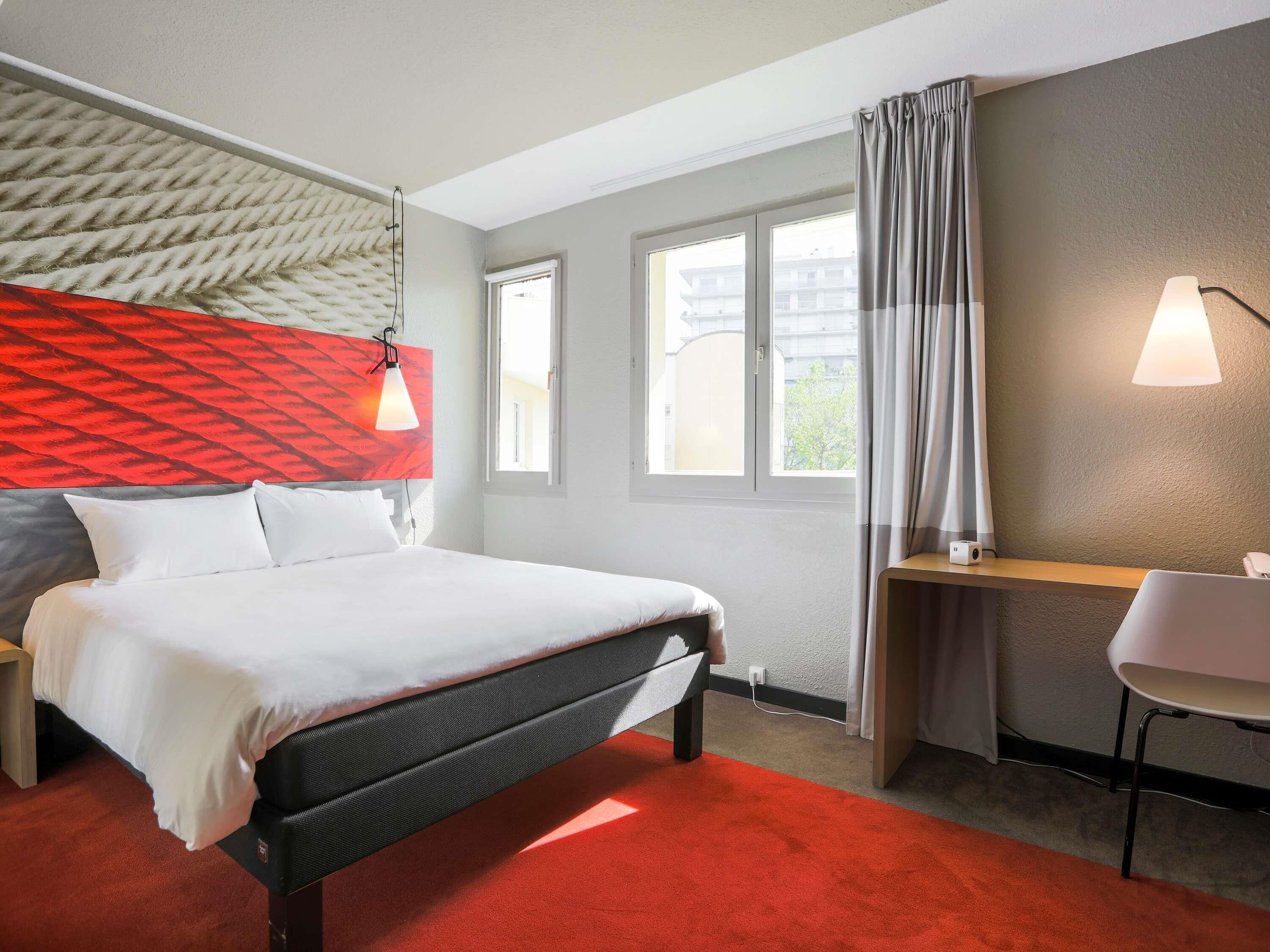 Ein Hotelzimmer mit Bett, Schreibtisch, Stuhl, Fenster und Lampe.