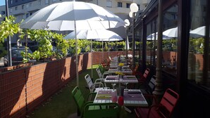 Een terras met tafels en stoelen, parasols en een bakstenen muur.