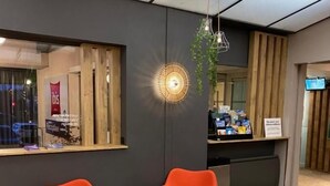 Een receptiegedeelte met twee oranje fauteuils, een kleine ronde tafel, een hanglamp en een houten balie met een bord.