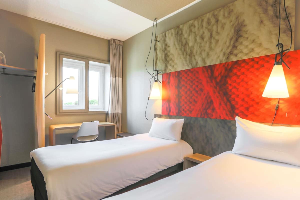 A hotel room with two beds, a desk, and a chair.