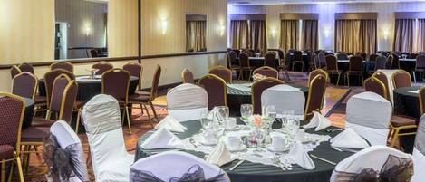 A banquet hall with round tables set for dining, chairs with white and black bows, and a carpeted floor.