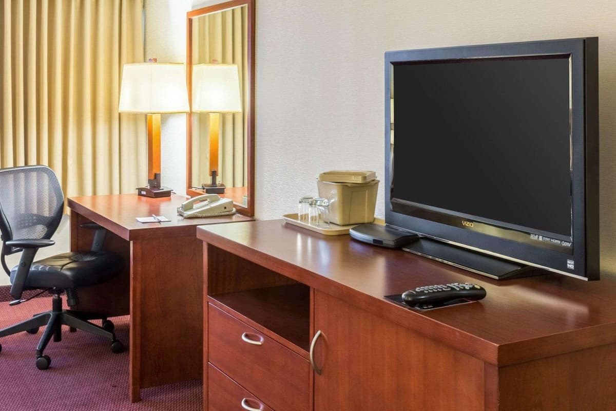 A hotel room with a wooden desk, a television, a chair, a lamp, a mirror, and a telephone.