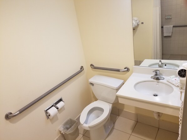 A bathroom with a toilet, a sink, a hand dryer, and a trash bin.