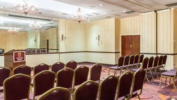 A conference room with rows of purple chairs, a podium with the Clarion Hotel logo, and a large mirror on the wall.