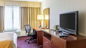 Une chambre d’hôtel avec un lit, un bureau avec une télévision, une chaise, une lampe et une fenêtre avec des rideaux.