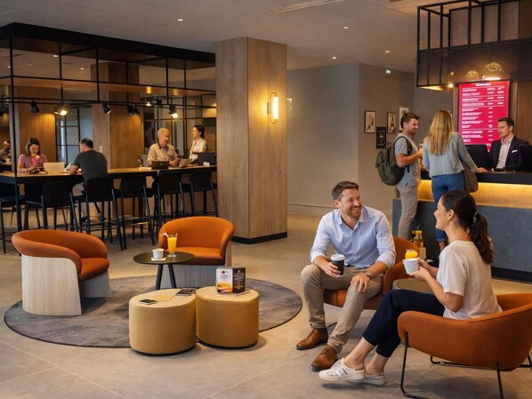 Un moderno vestíbulo de hotel con mesas redondas, asientos cómodos y una recepción.