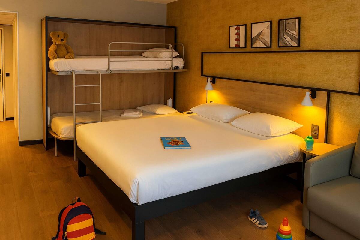 A hotel room with a bunk bed, a single bed, a teddy bear, a lamp, and a small table.