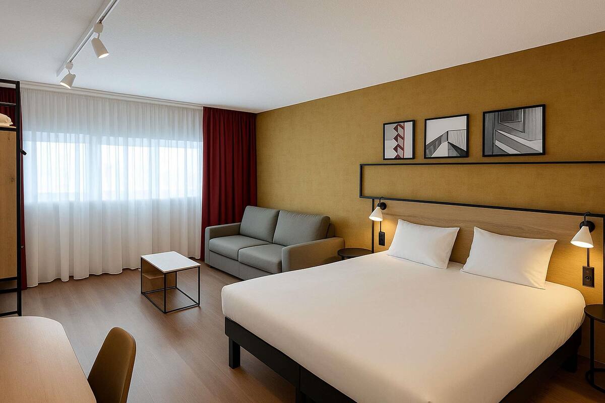 A hotel room with a bed, a sofa, a small table, and a desk. There are three wall-mounted picture frames.