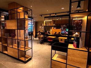 A modern interior with wooden shelving units, tables, and chairs arranged for dining or socializing. - Ibis Rungis Aéroport Paris Orly (Rungis)