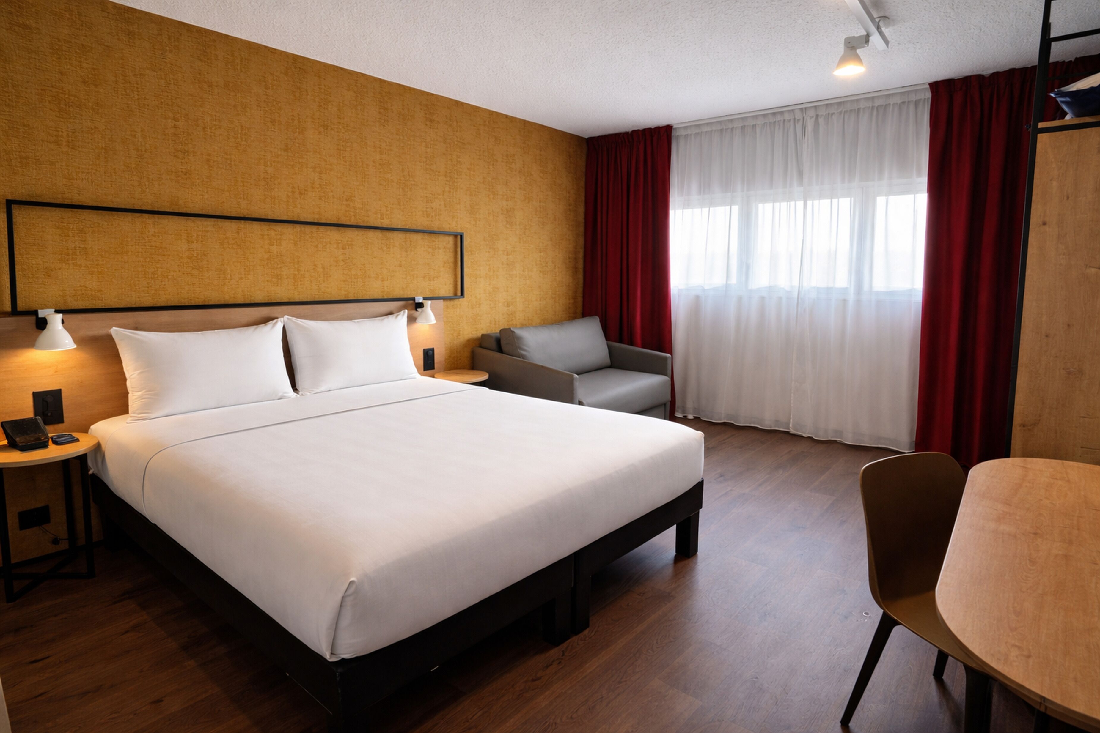 A hotel room with a large bed, a desk, a chair, and a sofa.