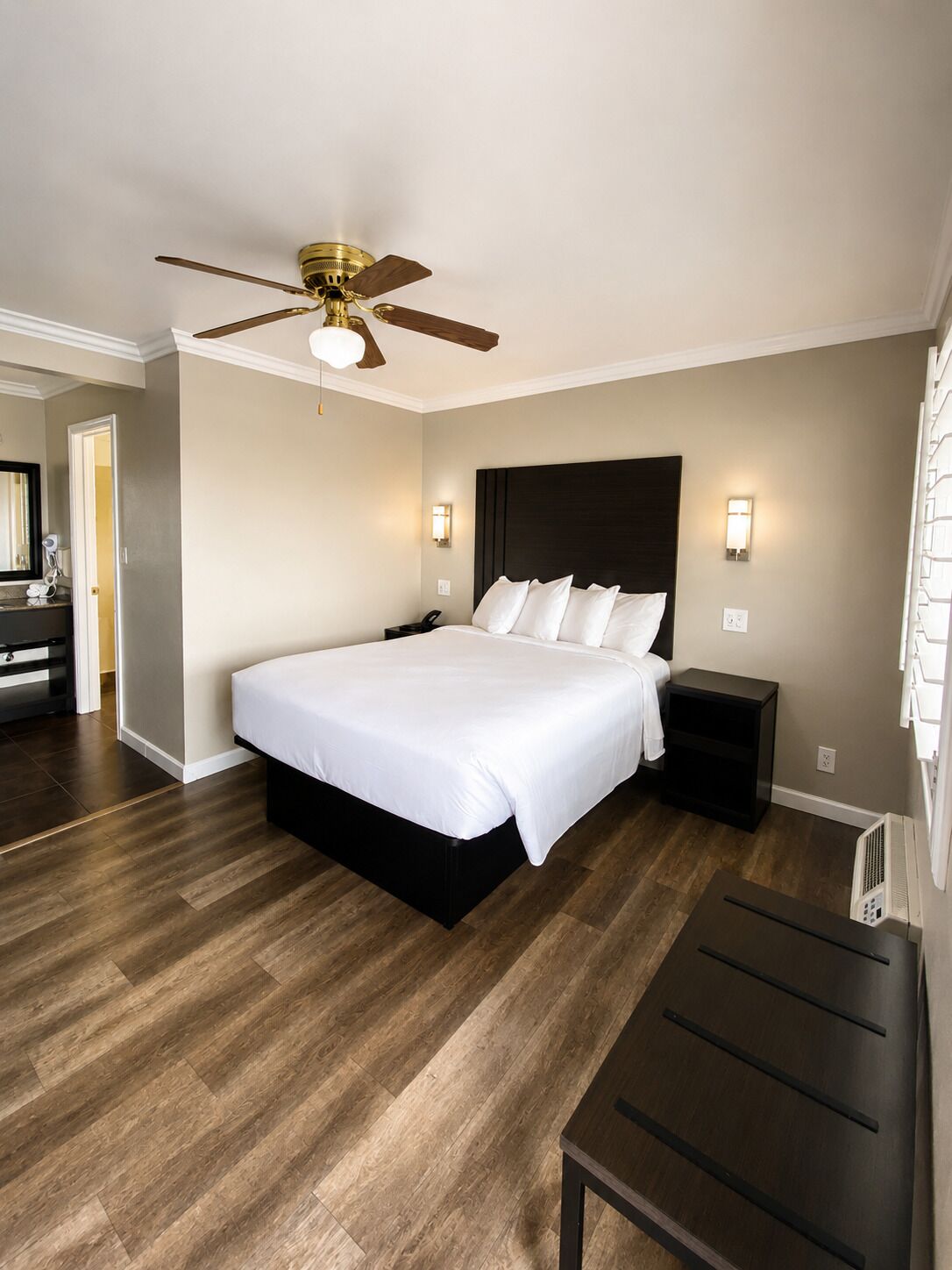 A bedroom with a bed, a nightstand, a desk, a ceiling fan, and a wall-mounted light fixture.