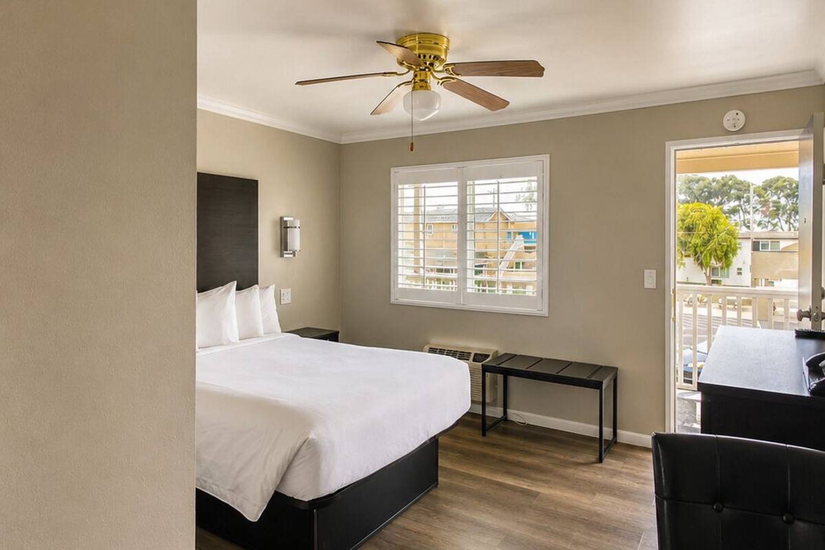 Une chambre d’hôtel équipée d’un lit, d’un bureau, d’une chaise, d’un ventilateur de plafond, d’une fenêtre et offrant une vue sur l’extérieur.