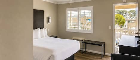 Una camera d'albergo con un letto, una scrivania, una sedia, una ventola a soffitto, una finestra e vista sull'esterno.