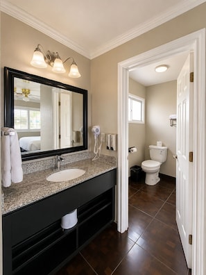 A bathroom with a large mirror, two wall-mounted lights, a sink, a toilet, and a shower area. - Rockview Inn and Suites - Morro Bay CA (Morro Bay)