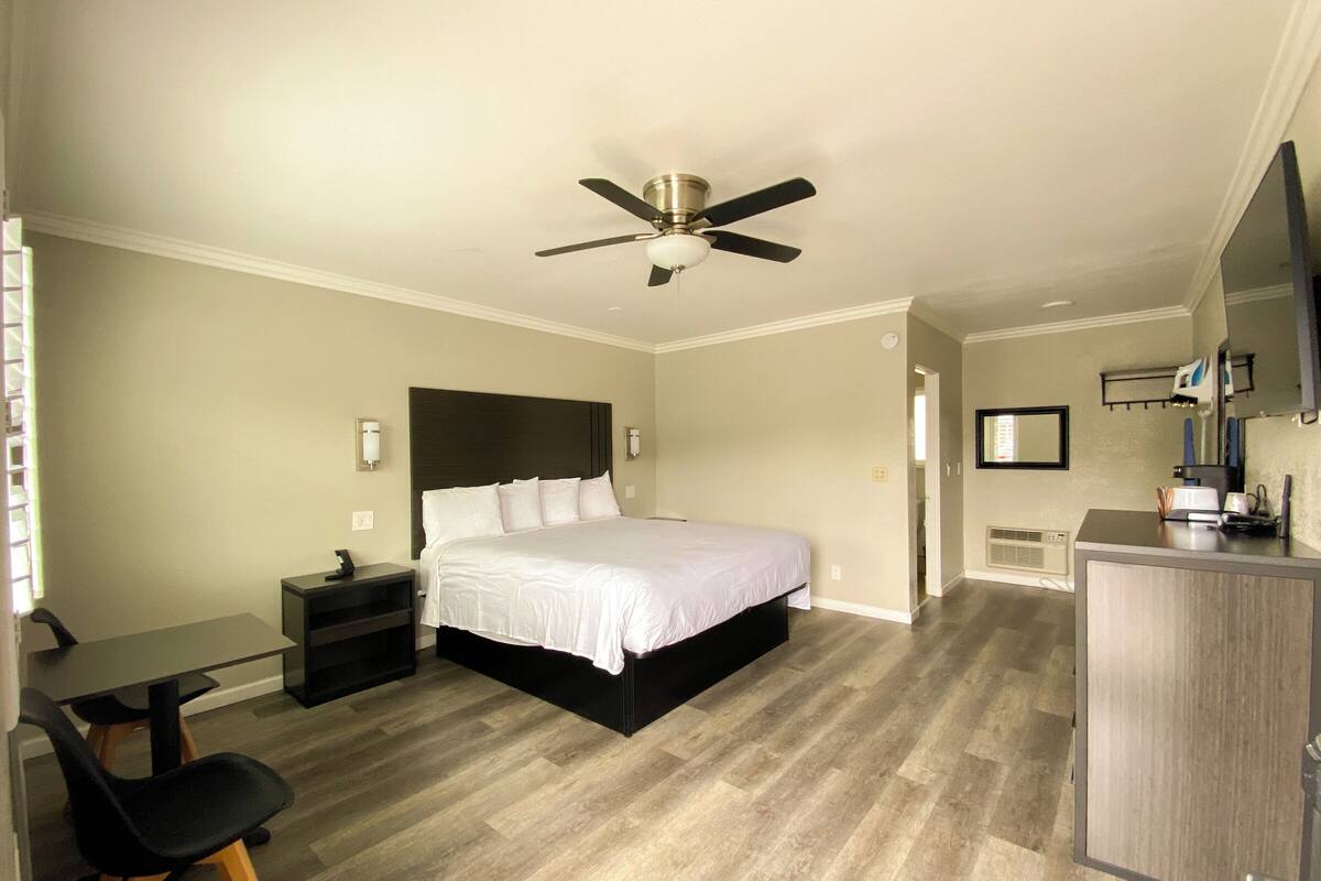 Une chambre d’hôtel équipée d’un lit, d’un bureau, d’une chaise, d’un ventilateur de plafond et d’une télévision.