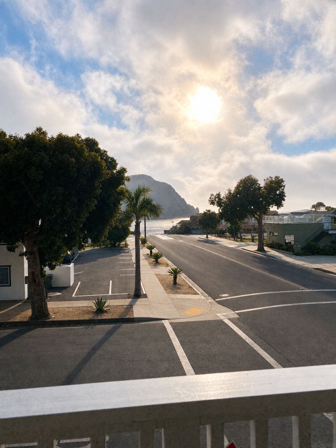 A street view with a clear sky, a mountain in the distance, and a building with a balcony.