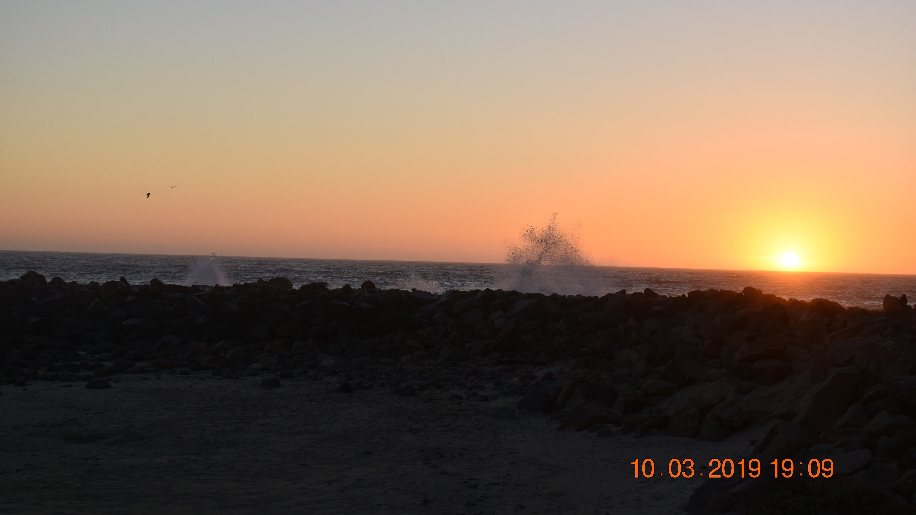 A beach scene with waves crashing against rocks at sunset.