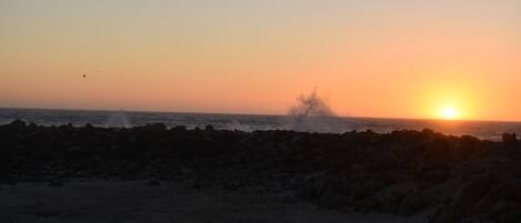 A beach scene with waves crashing against rocks at sunset.