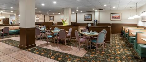 Un restaurante con cabinas y mesas, alfombra floral e iluminación en el techo.