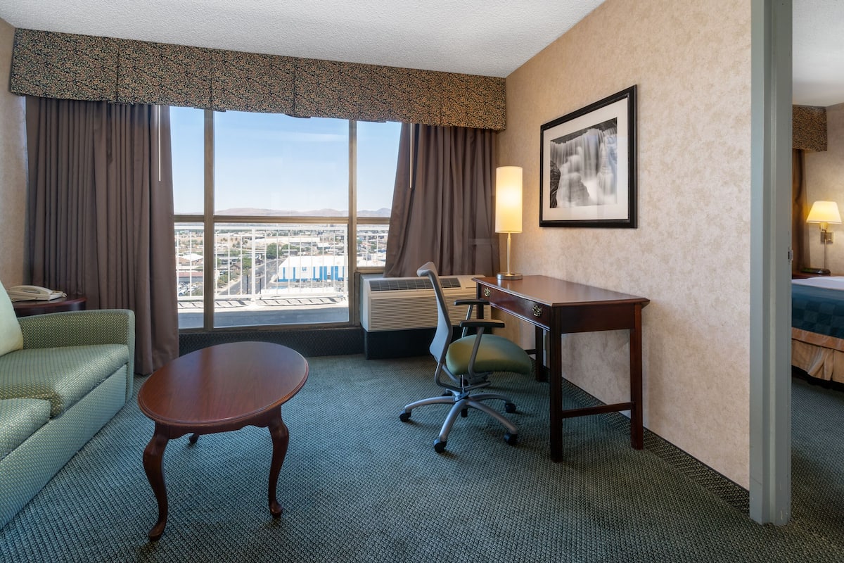 A hotel room with a large window, a desk, a chair, a sofa, and a bed.