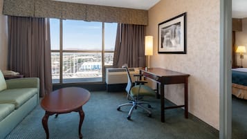 A hotel room with a large window, a desk, a chair, a sofa, and a bed.