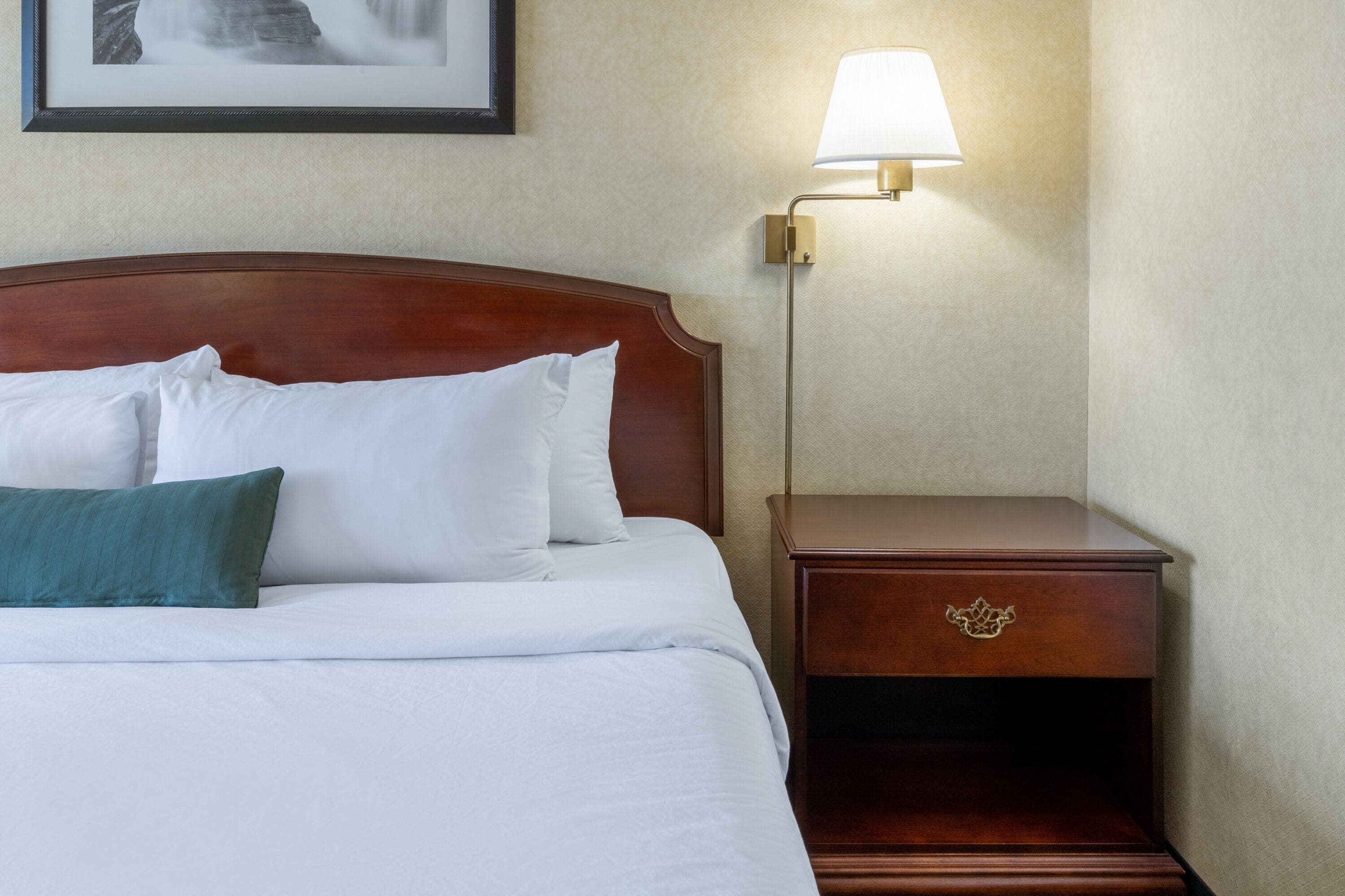 A neatly made bed with white and teal pillows, a wooden headboard, and a bedside table with a lamp.