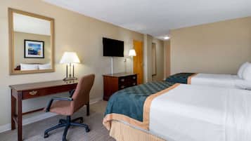 A hotel room with a desk, two beds, a TV, and a lamp.