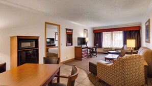 A hotel room with a dining table, a sofa, a TV, a desk, and a window with curtains. - SureStay by Best Western Miles City (Miles City)