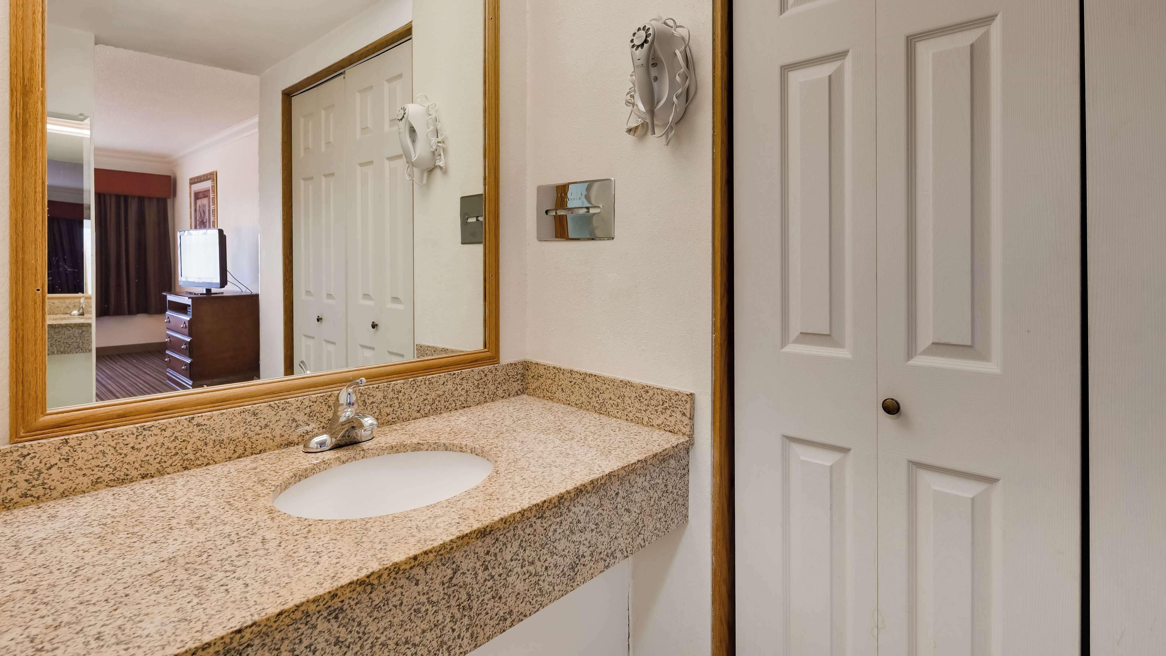 A bathroom with a granite countertop sink, a large mirror, and a white door.