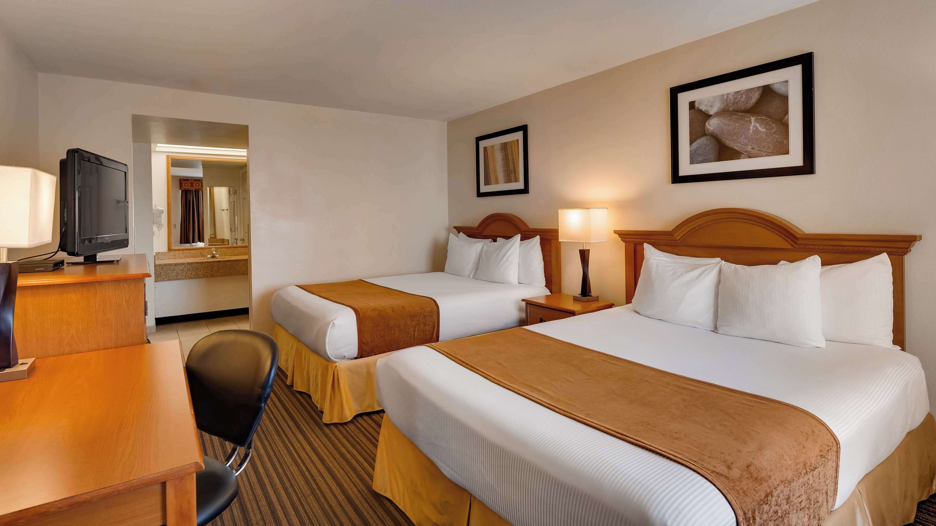 A hotel room with two beds, a desk, a chair, a television, and a framed picture on the wall.