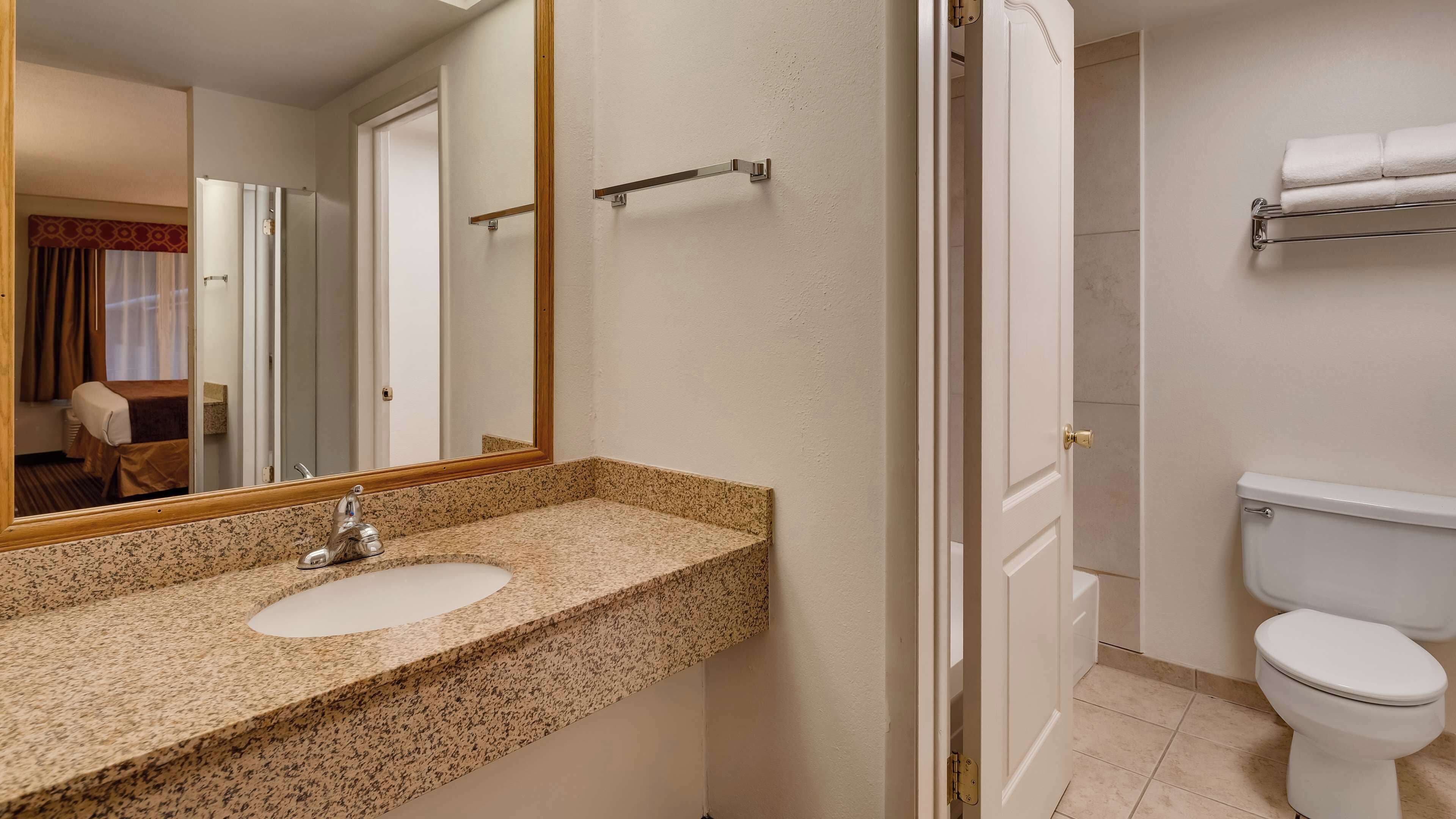 A bathroom with a granite countertop sink, a mirror, a towel rack, and a toilet.