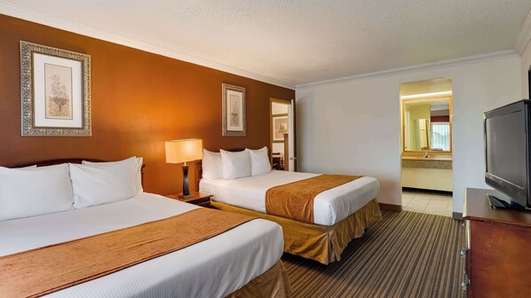 Une chambre d’hôtel avec deux lits, une télévision et une salle de bain visible à travers une porte ouverte.