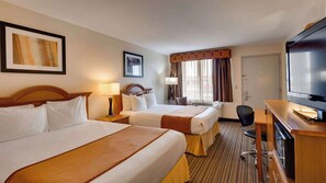 A hotel room with two beds, a desk with a television, a chair, and a window with curtains. - SureStay by Best Western Miles City (Miles City)