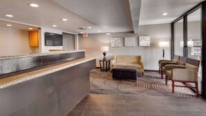 A reception area with a counter, a television, a sofa, and a patterned rug. - SureStay by Best Western Miles City (Miles City)
