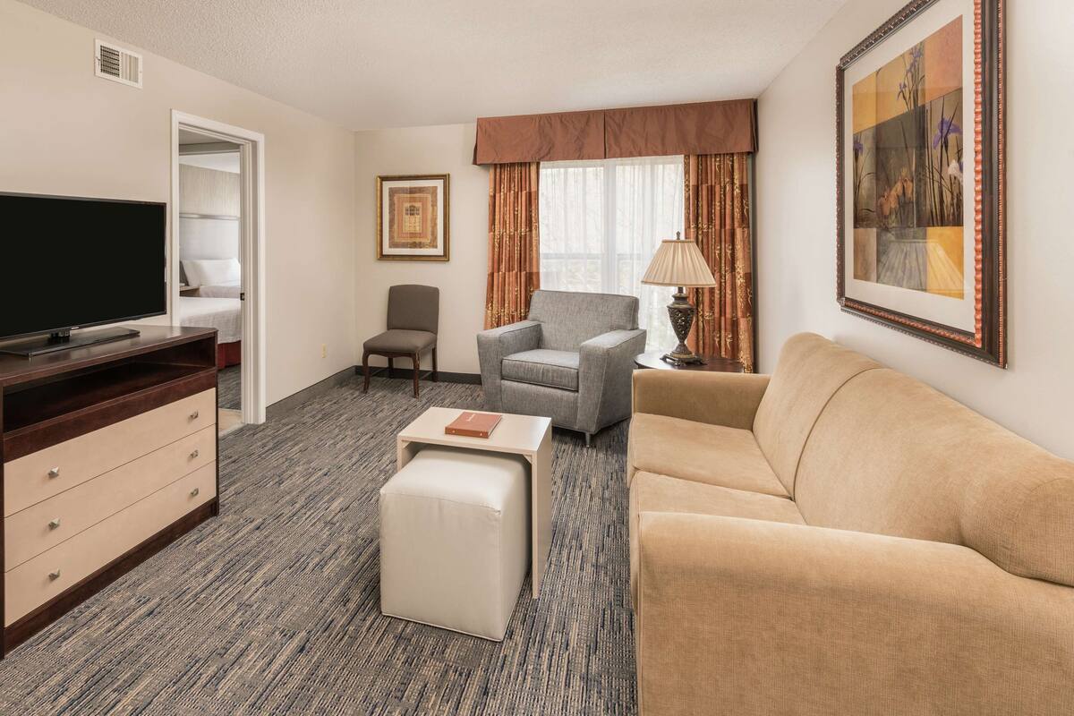 Une chambre d’hôtel équipée d’un téléviseur à écran plat, d’un canapé, d’un fauteuil, d’une petite table et d’une lampe.