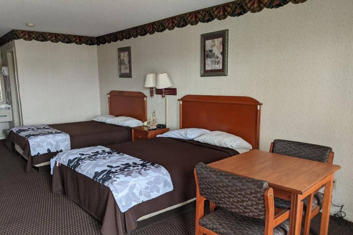 A hotel room with two beds, a wooden table, and a chair.
